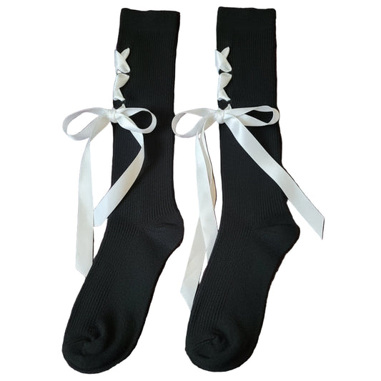 Black knee-high socks with white ribbons laid on a bed with a fluffy purple bedspread