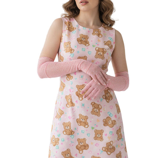 Pink arm sleeves with embellishments on a girl with a pink teddy bear dress in a white room