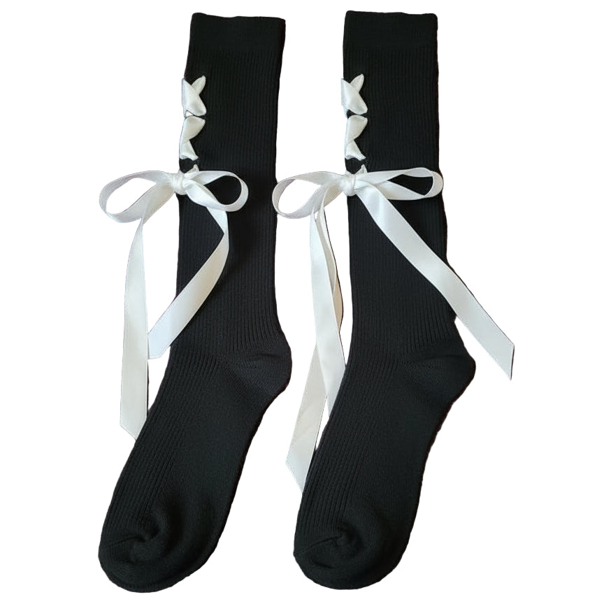 Black knee-high socks with white ribbons laid on a bed with a fluffy purple bedspread 