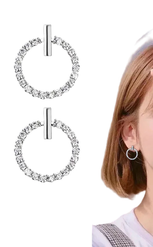 Silver hoop earrings with clear stones on a black background, worn by a person outdoors.