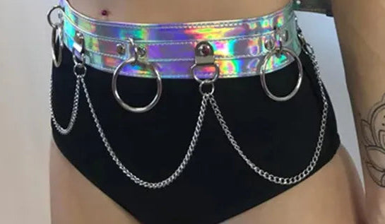 Person wearing a shiny, iridescent harness and black high-waisted bottoms with chain details.