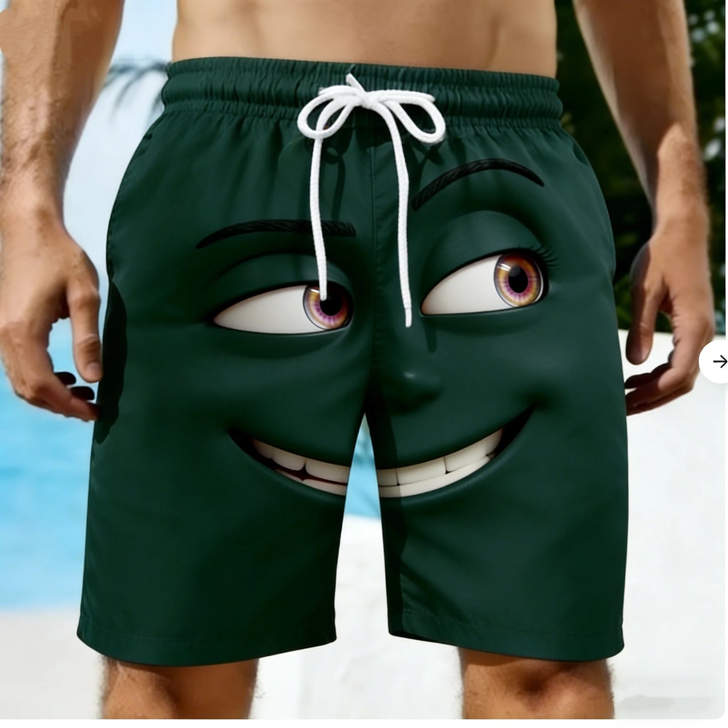 Green swim shorts with a cartoon face design on a beach.