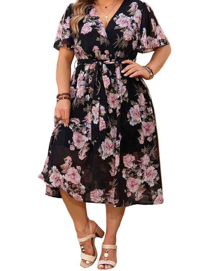 Woman wearing a floral dress standing outdoors with plants and flowers in the background