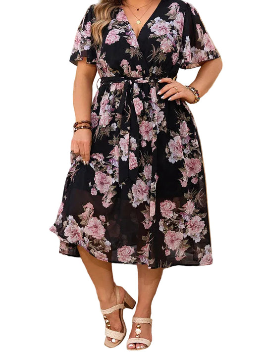 Woman wearing a floral dress standing outdoors with plants and flowers in the background