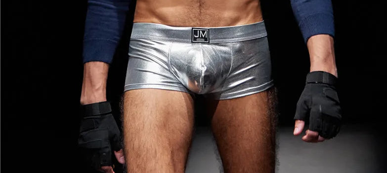 Person wearing a blue long-sleeve shirt, black face covering, and silver underwear against a dark background.