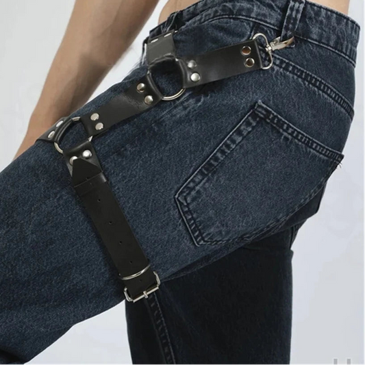Person wearing dark blue jeans with a black leather harness on a plain background