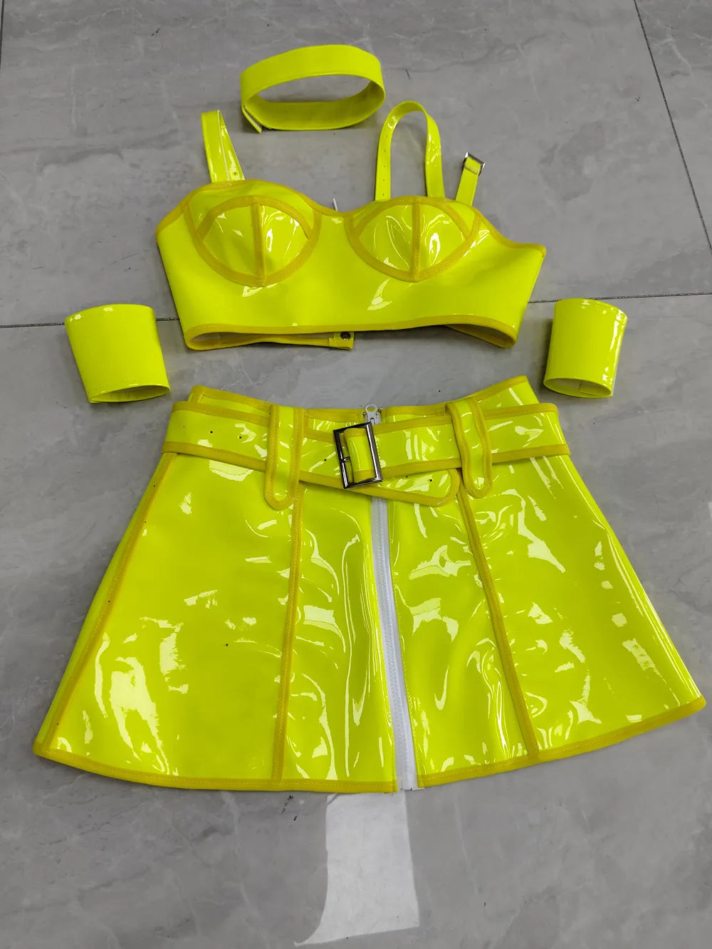Neon yellow vinyl outfit with top, skirt, and accessories on a gray floor.