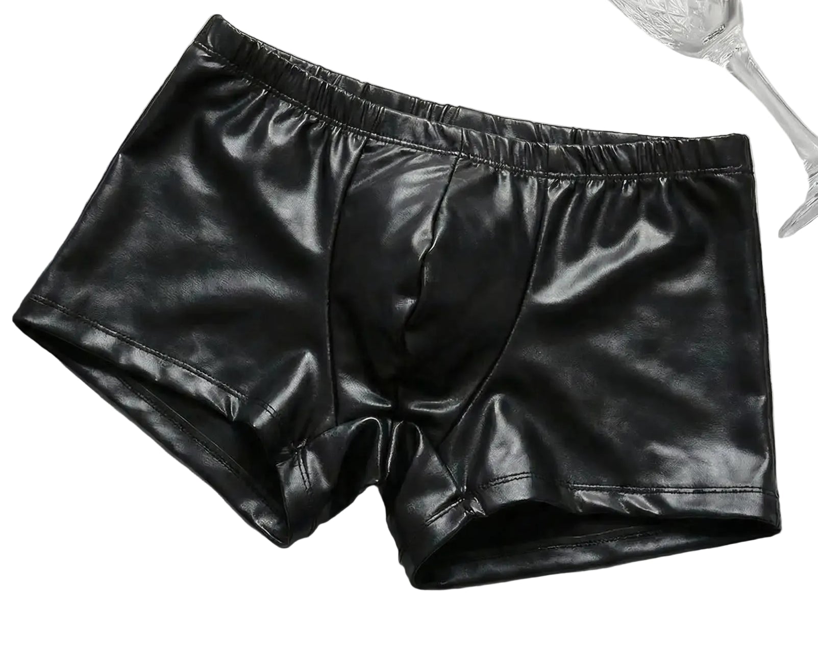 Black leather shorts on a textured white surface with a glass of champagne and newspaper.