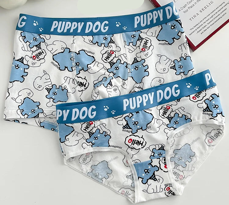 Two pairs of 'Puppy Dog' patterned underwear on a white surface with a book and candle in the background.