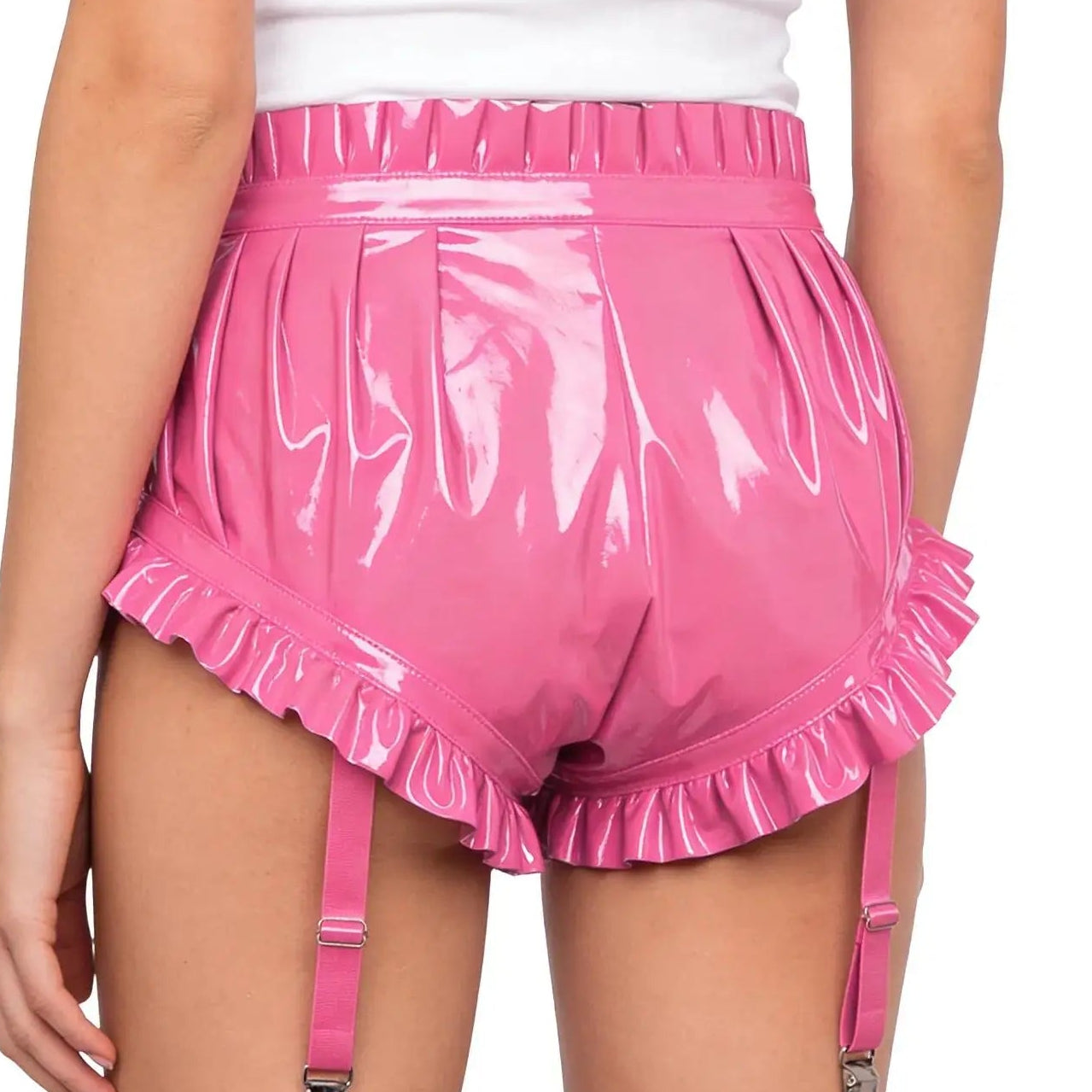 Person wearing pink vinyl shorts with ruffles and suspenders on a white background