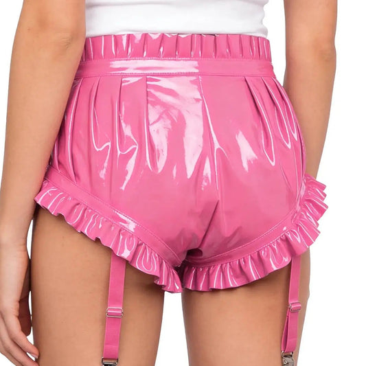 Person wearing pink vinyl shorts with ruffles and suspenders on a white background