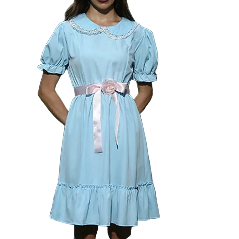 Person wearing a light blue dress with a pink belt, standing outdoors with a skeleton and spider web in the background.